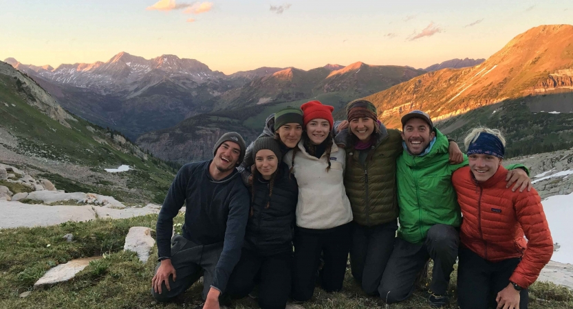 A group of people smile for a photo in front of a vast mountainous landscape. 